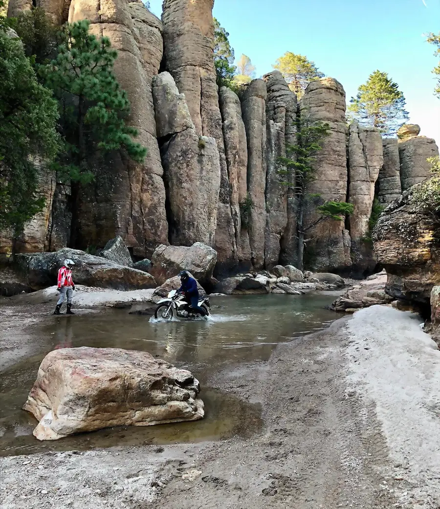 Dirt bike crossing a stream below rock spires